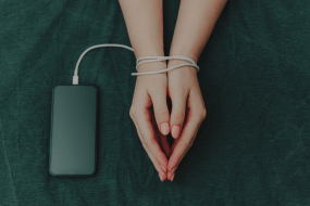 Manos atadas con cable a un dispositivo, simbolizando dependencia digital y uso excesivo de tecnología