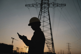 Persona usando el móvil en entorno industrial con torres eléctricas, representando conexión digital y tecnología