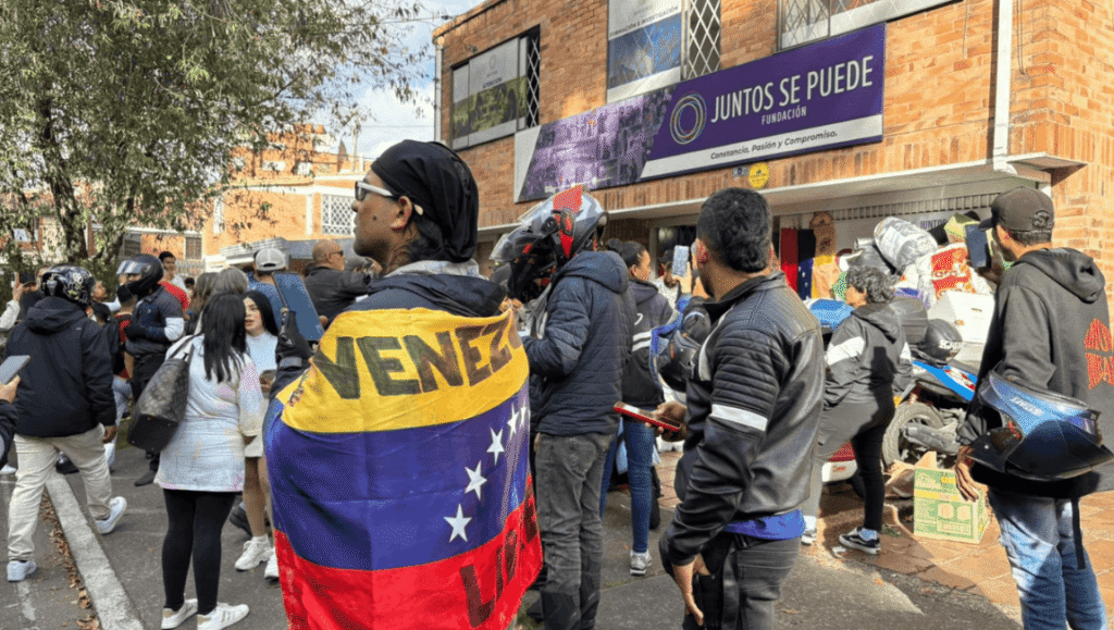 Grupo de ciudadanos reunidos frente a la Fundación Juntos Se Puede, con personas portando la bandera de Venezuela y organizando cajas de donaciones y ayuda humanitaria en la calle.