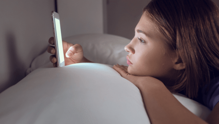 Mujer acostada mirando el celular de noche con expresión pensativa