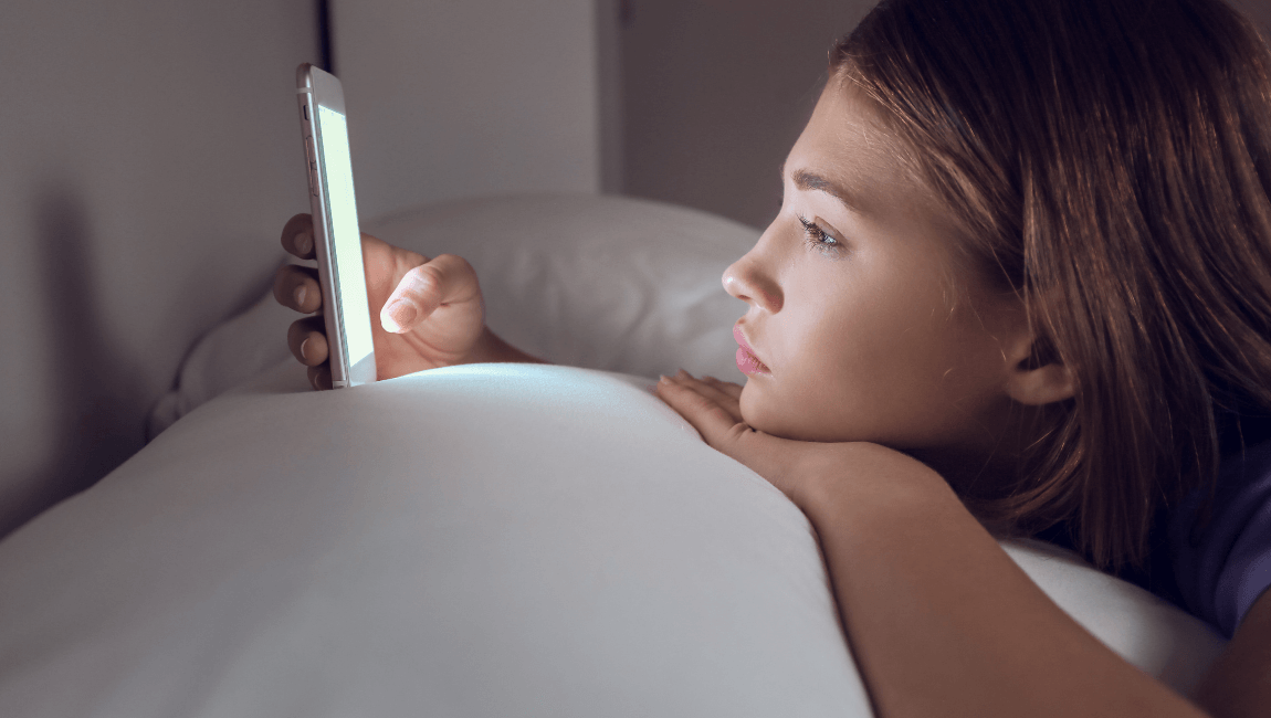Mujer acostada mirando el celular de noche con expresión pensativa