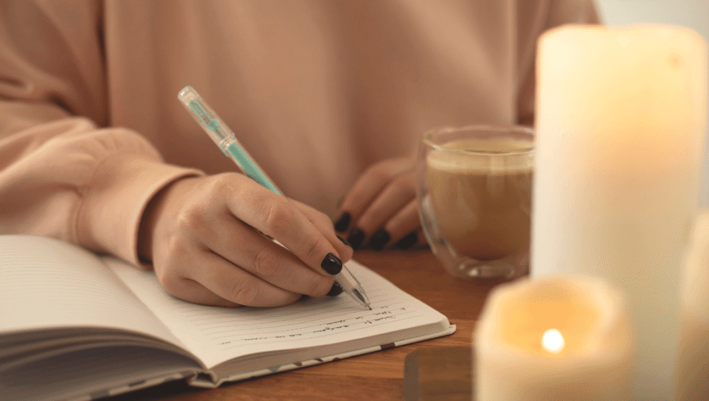 Cuaderno abierto con un bolígrafo, una planta pequeña y luz natural sobre una superficie neutra.