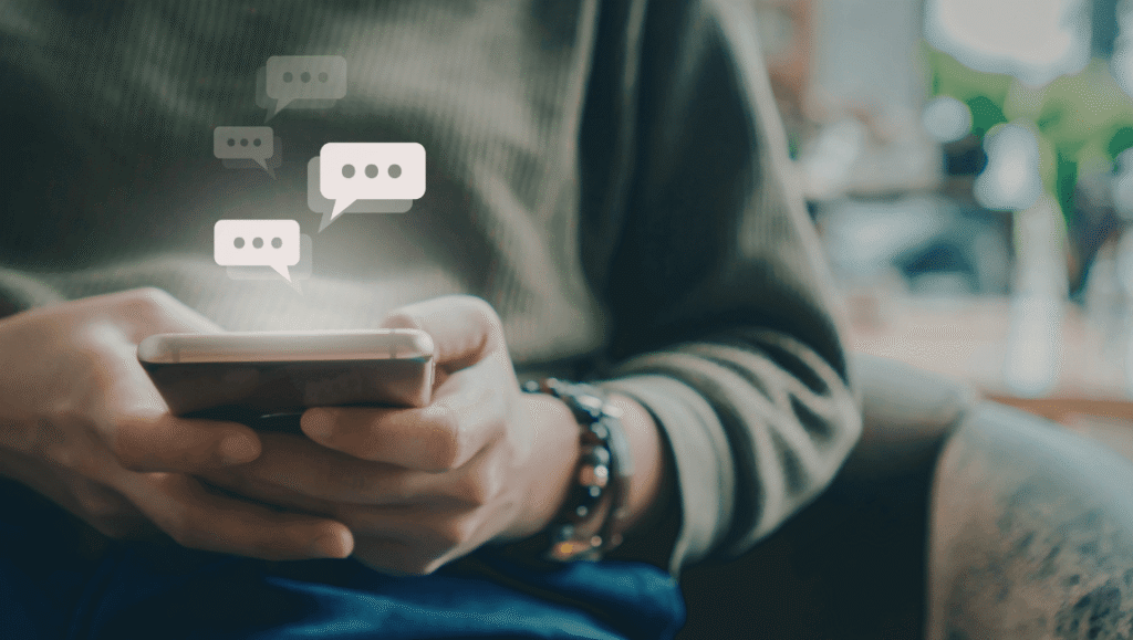 Primer plano de unas manos sosteniendo un teléfono celular con notificaciones y mensajes flotantes, representando la sobrecarga digital y la presión de los chats.