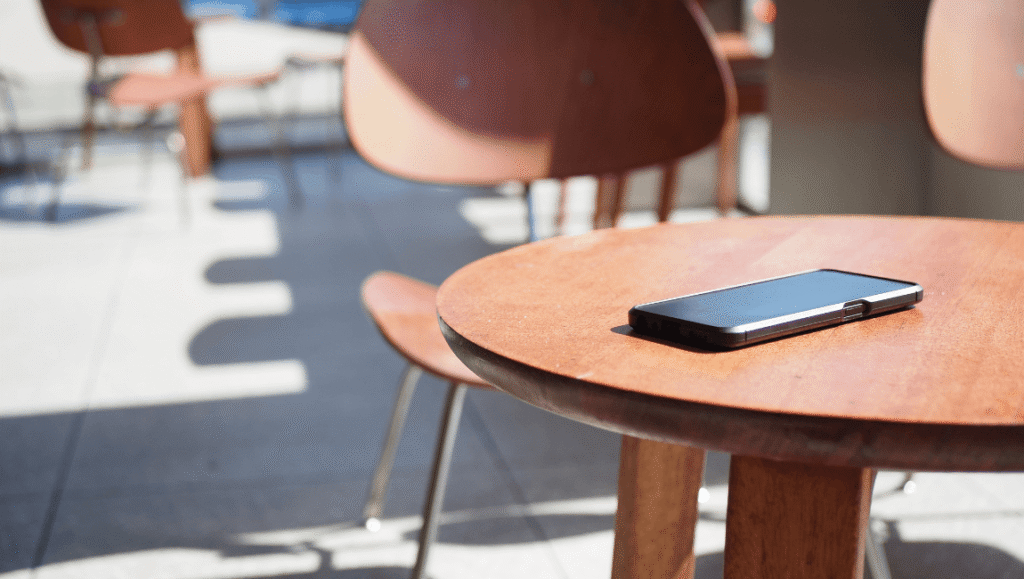 Celular apagado sobre una mesa de madera en una terraza, sin nadie mirándolo